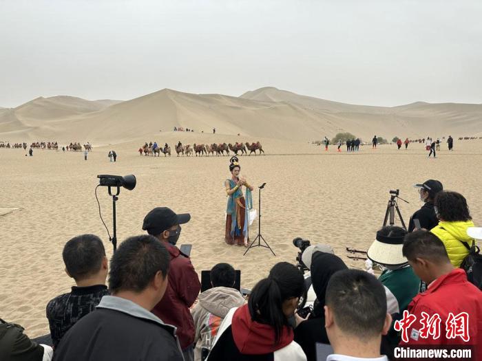 圖為2023年4月底，敦煌大漠“逐舞者”奧楠在鳴沙山月牙泉景區(qū)視頻直播，吸引游人圍觀。　馮志軍 攝